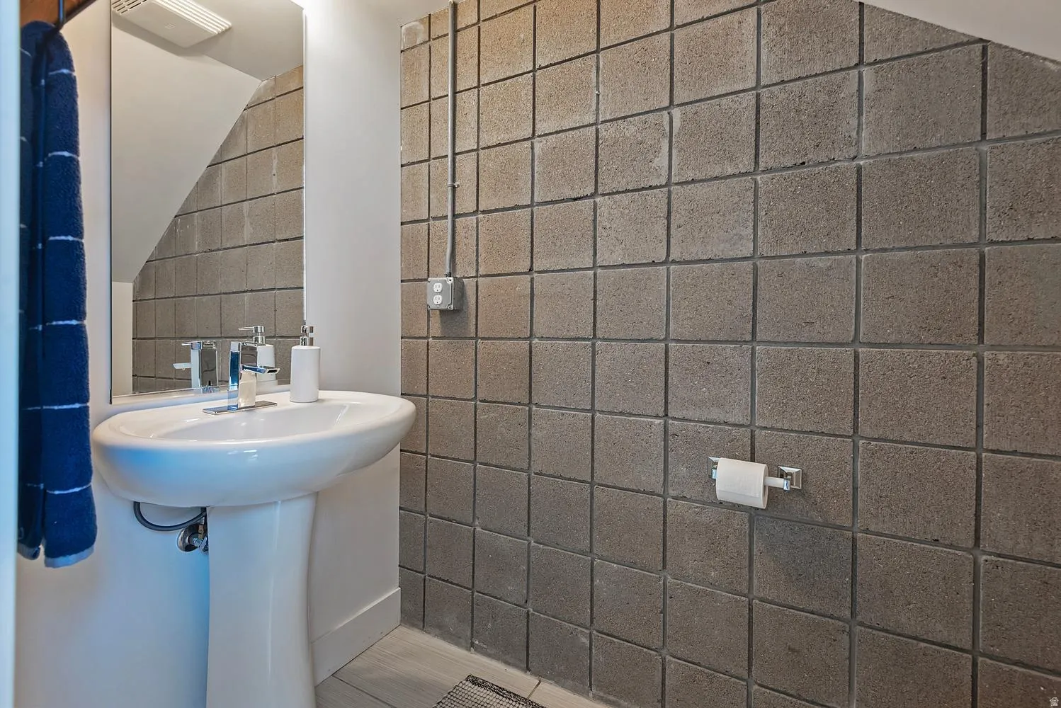 Pedestal sink with chrome faucet, mirror, textured wall tiles, and built-in wall electrical conduit
