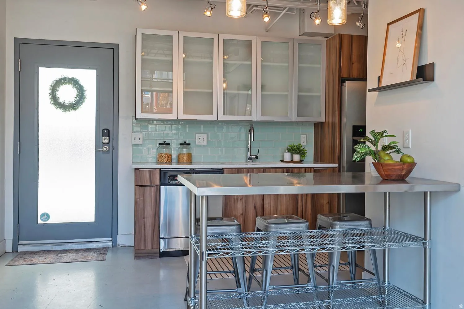 Modern kitchen featuring a stainless steel countertop island, wood-finish lower cabinetry, frosted glass upper cabinets, a turquoise subway tile backsplash, and stainless steel appliances