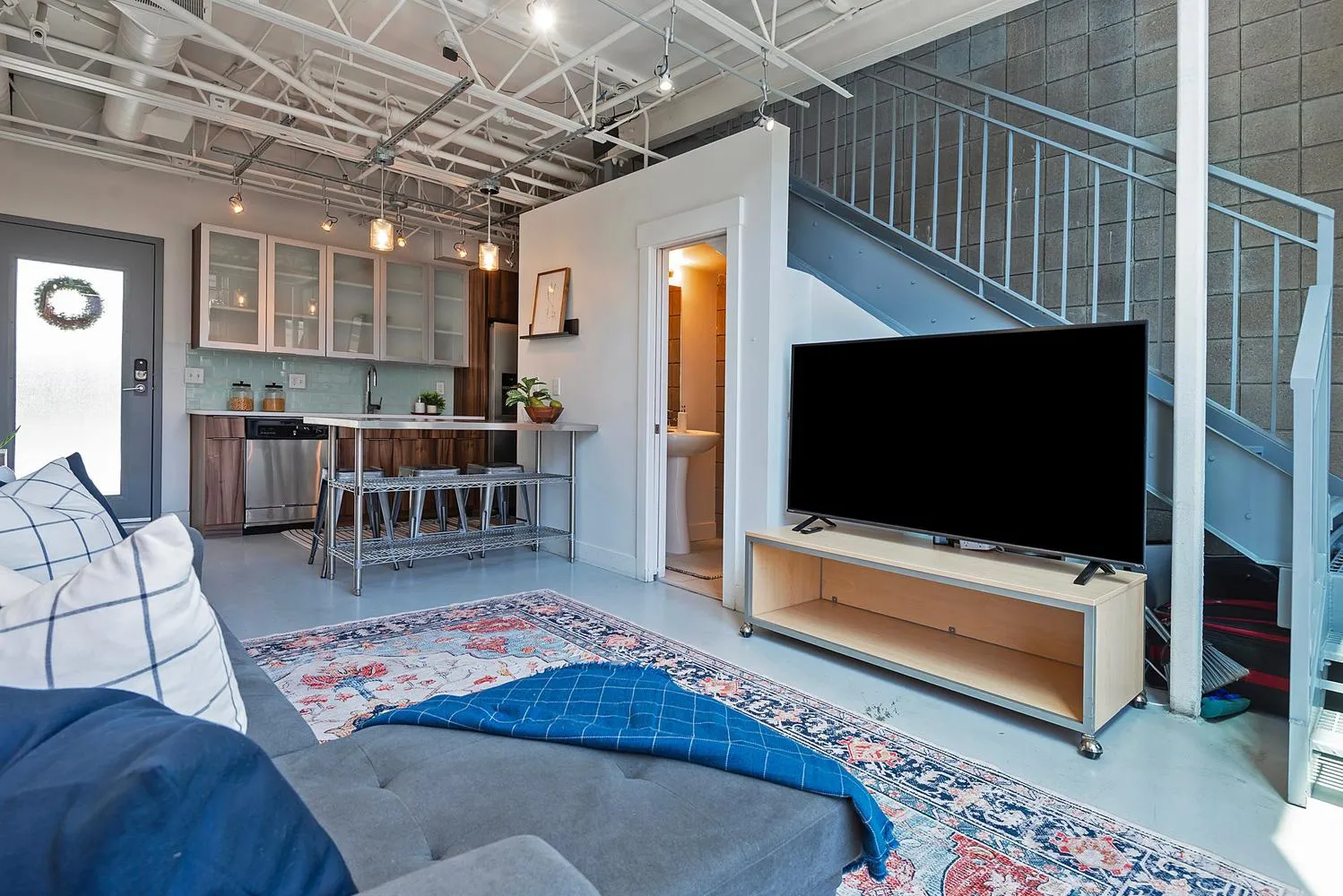 Open-concept living space featuring exposed ceiling ductwork, concrete flooring, and a metal staircase with industrial railing