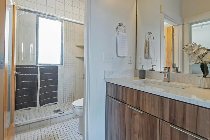 Bathroom vanity featuring a wood-finish cabinet with chrome hardware, an integrated rectangular sink, and a speckled light-toned countertop