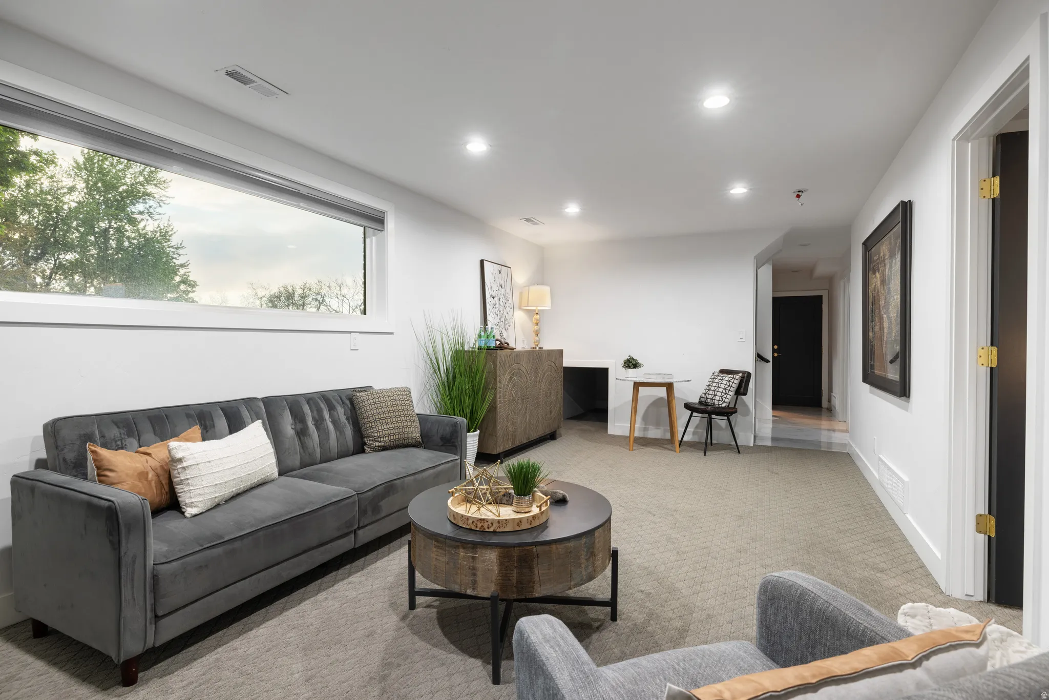 Spacious living area featuring a large horizontal window, recessed lighting, neutral carpeting, and white trim