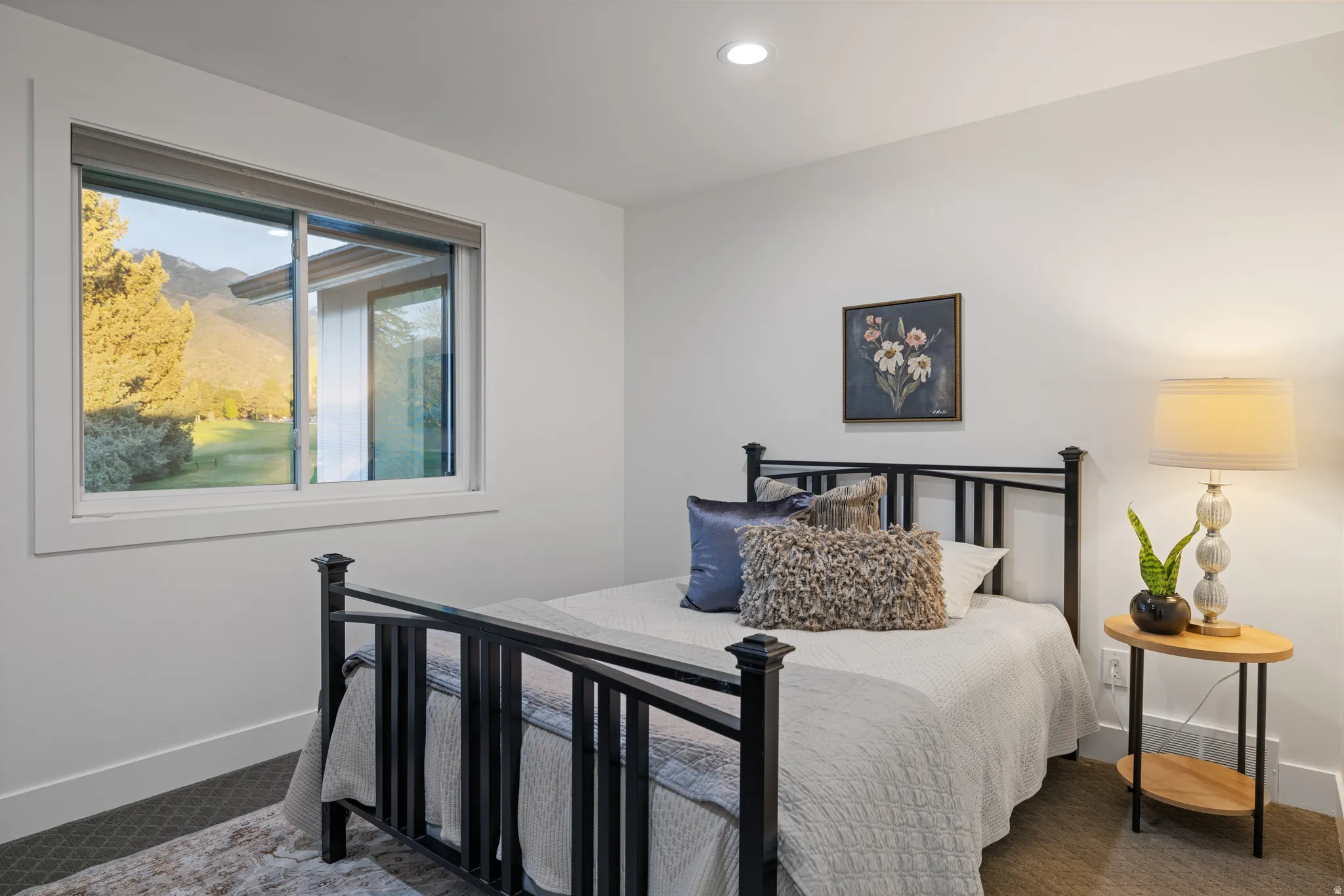 Bright bedroom featuring a large window with mountain scenery, recessed ceiling lighting, a dark metal bed frame, and carpet flooring