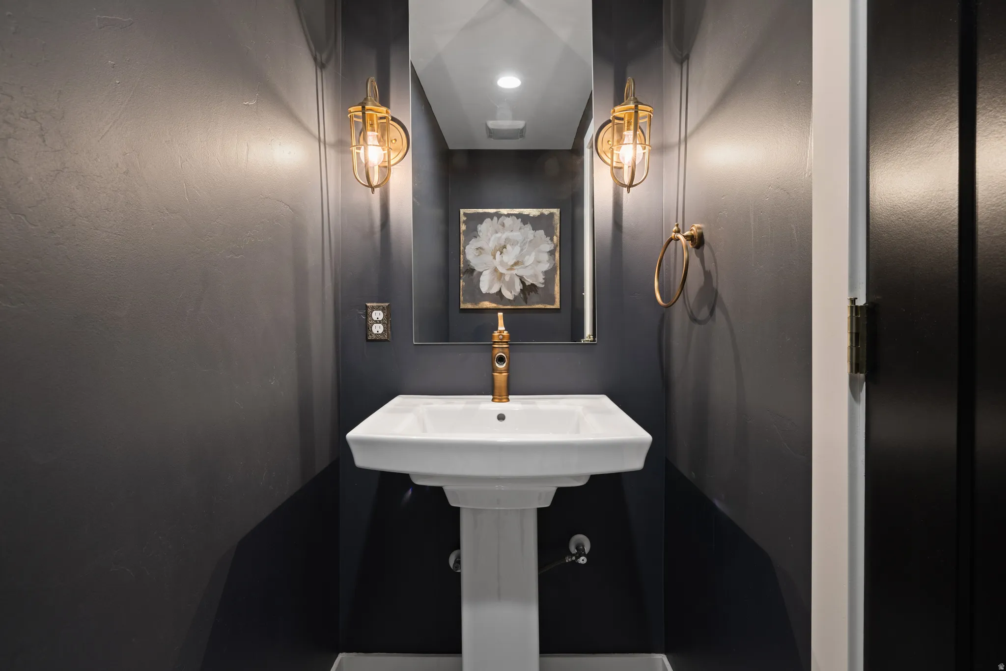 Pedestal sink with brass-finish faucet, framed mirror, and brass-finish sconces