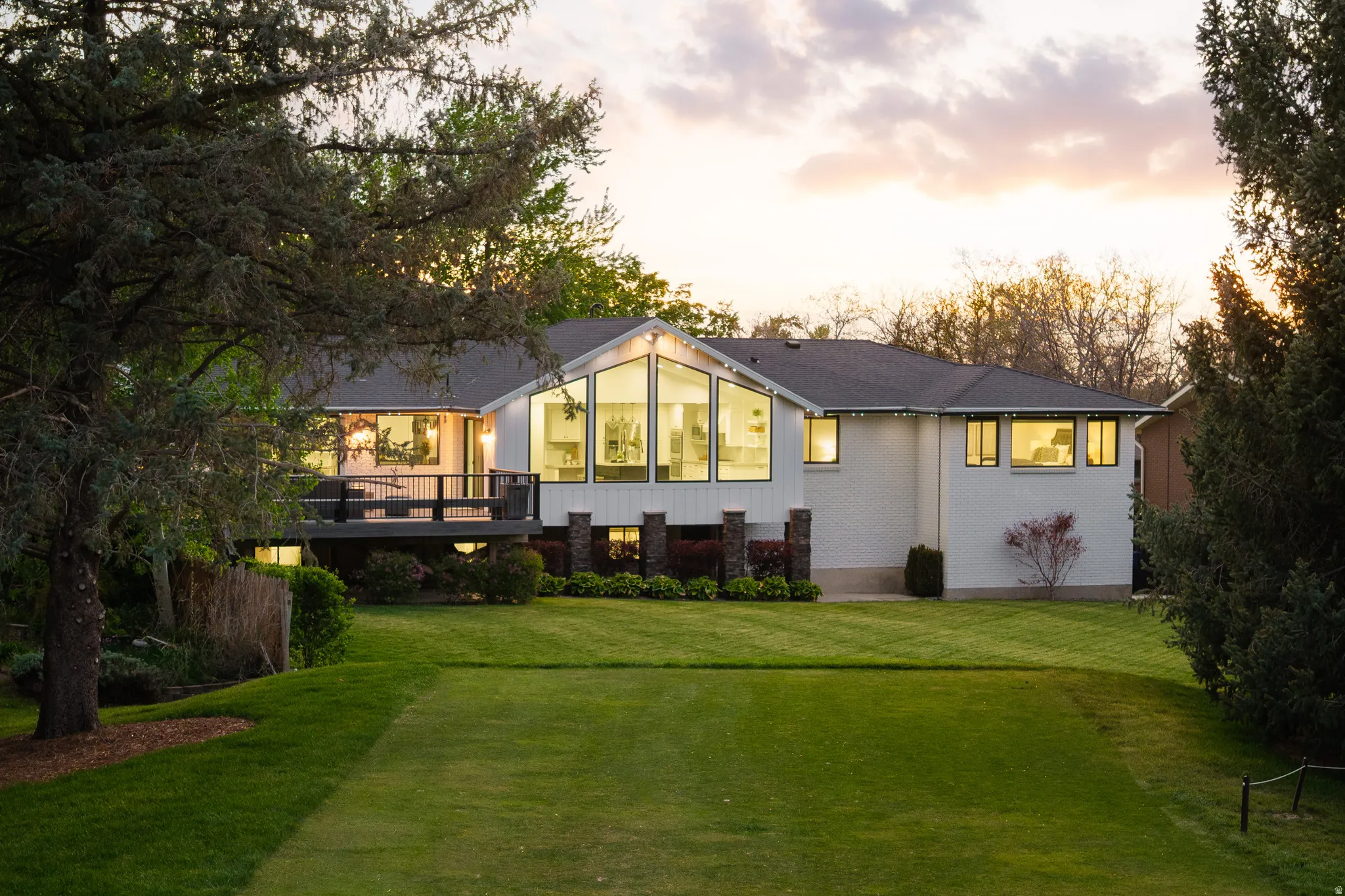 Rear exterior featuring a large, manicured lawn, a spacious deck with dark railing, and a gabled window wall with expansive glass