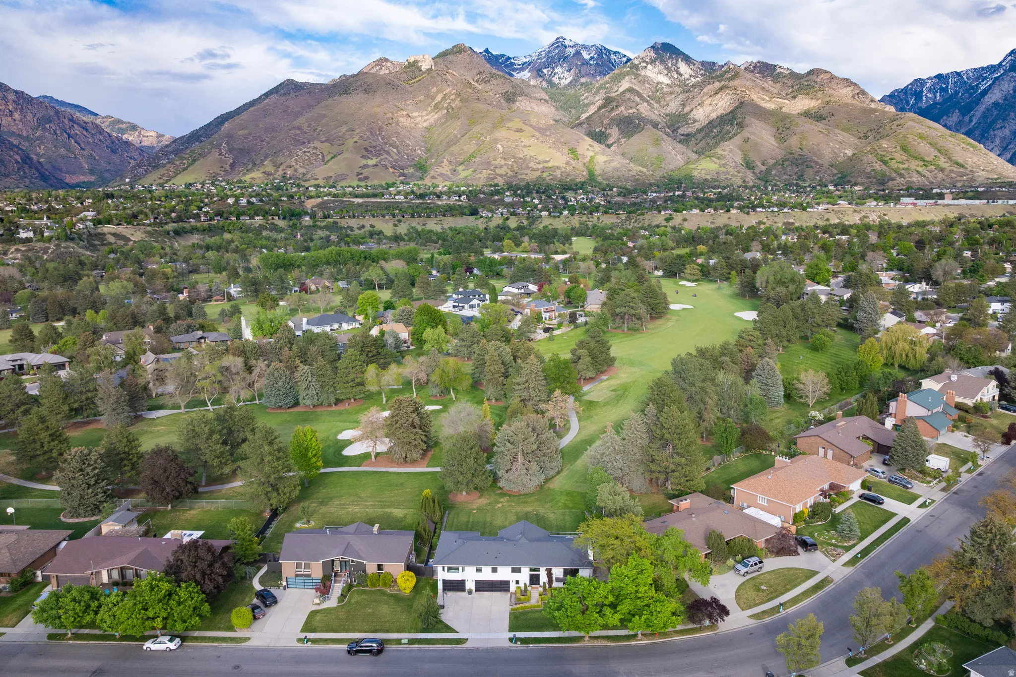 Expansive aerial landscape featuring snow-capped mountains, a verdant golf course, and mature trees