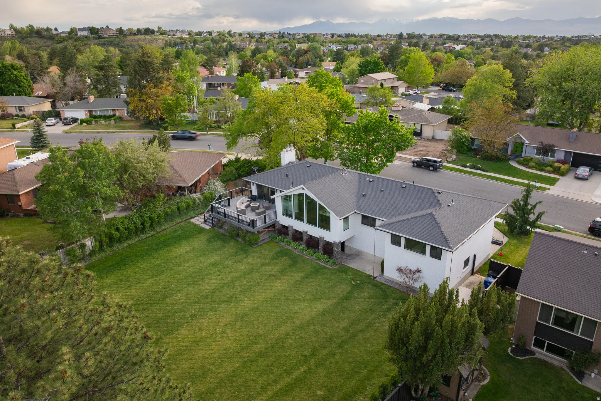 Contemporary residence featuring a spacious backyard with green lawn, an elevated deck, and mature landscaping