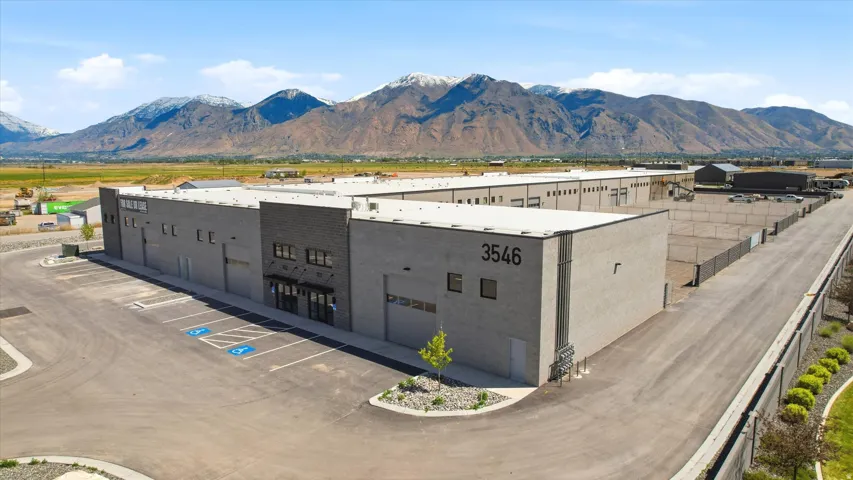 Modern commercial complex featuring a large paved parking area, multiple loading dock doors, and distinct dark brick and light concrete facade elements