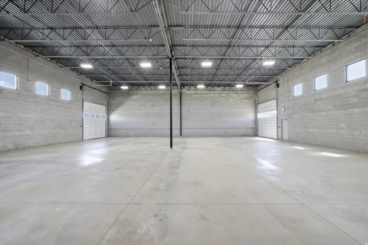 Expansive industrial space featuring concrete block walls, a high exposed ceiling with metal trusses, and polished concrete flooring