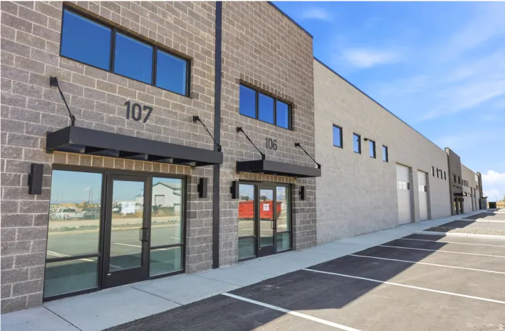 Modern commercial building featuring dark brick accents, large storefront windows, overhead awnings, and an expansive paved parking lot