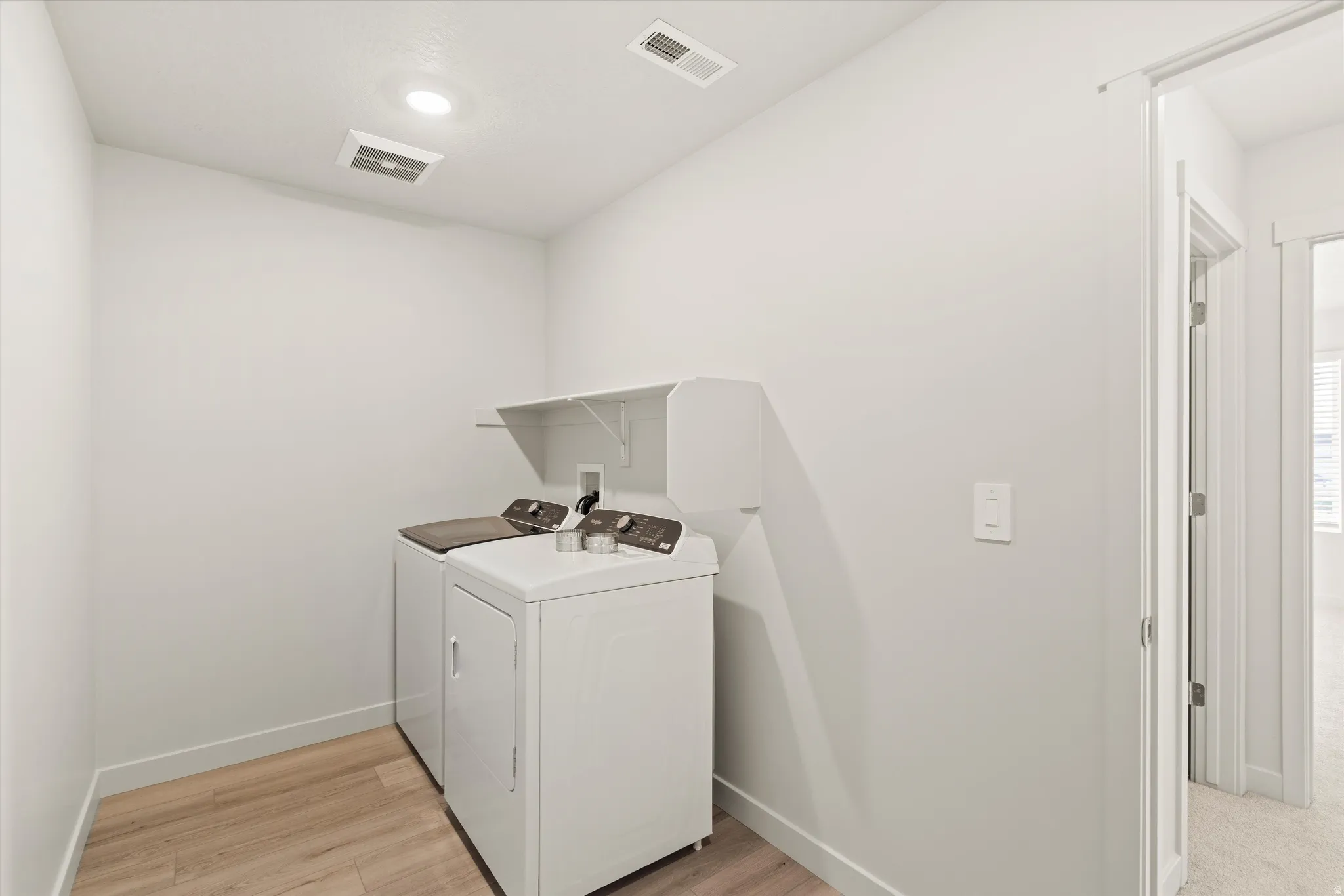 Dedicated laundry area featuring wood-finish flooring, white walls, and a built-in white shelving unit