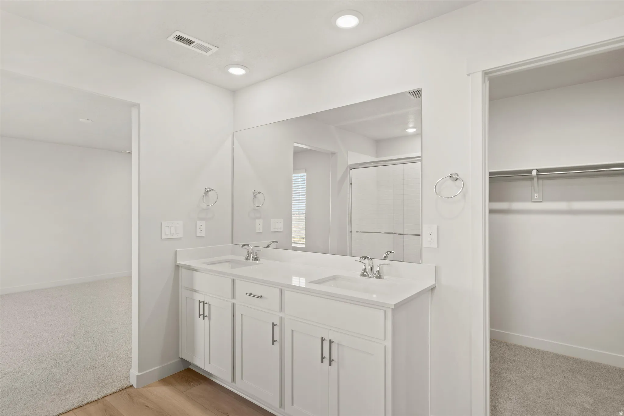 Bathroom featuring a dual vanity with white cabinetry, integrated sinks, chrome hardware, a large wall-mounted mirror, and recessed lighting