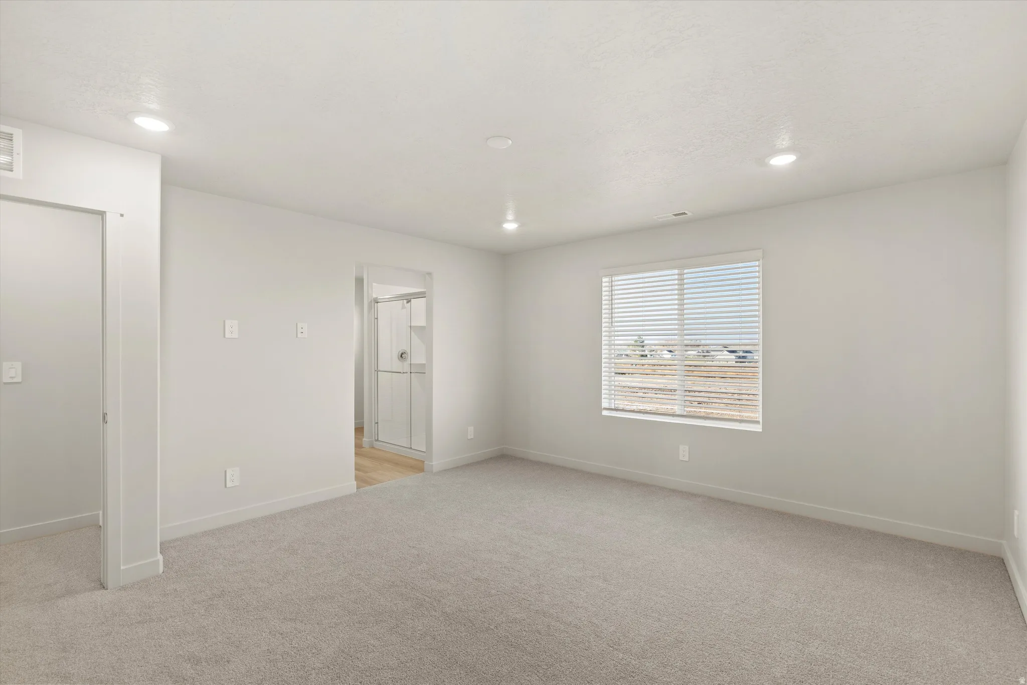 Spacious room featuring neutral carpeting, recessed lighting, and a large window with horizontal blinds