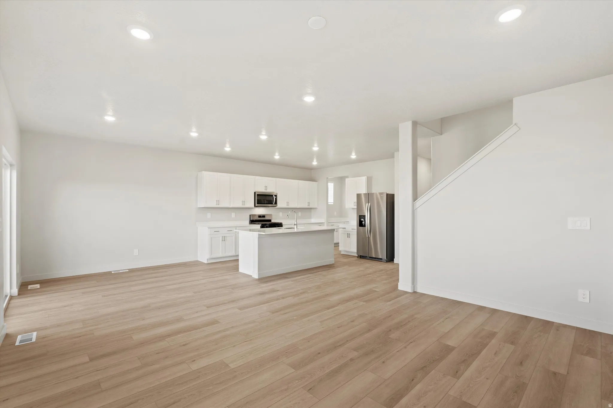 Open concept living space featuring light wood-finish flooring, recessed lighting, a modern kitchen with white cabinetry, a central island, and stainless steel appliances