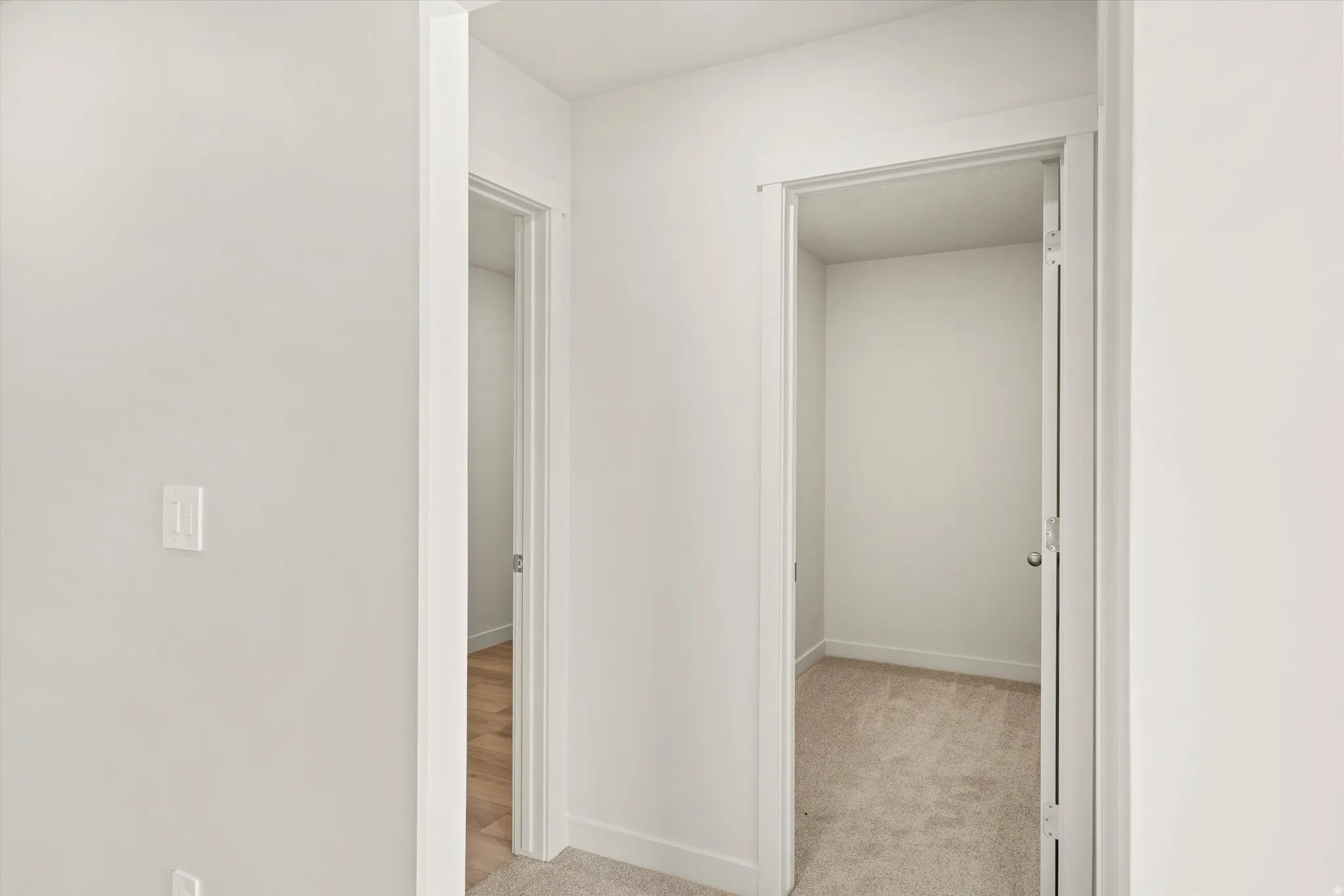 Hallway featuring neutral wall tones, white trim, and two recessed doorways