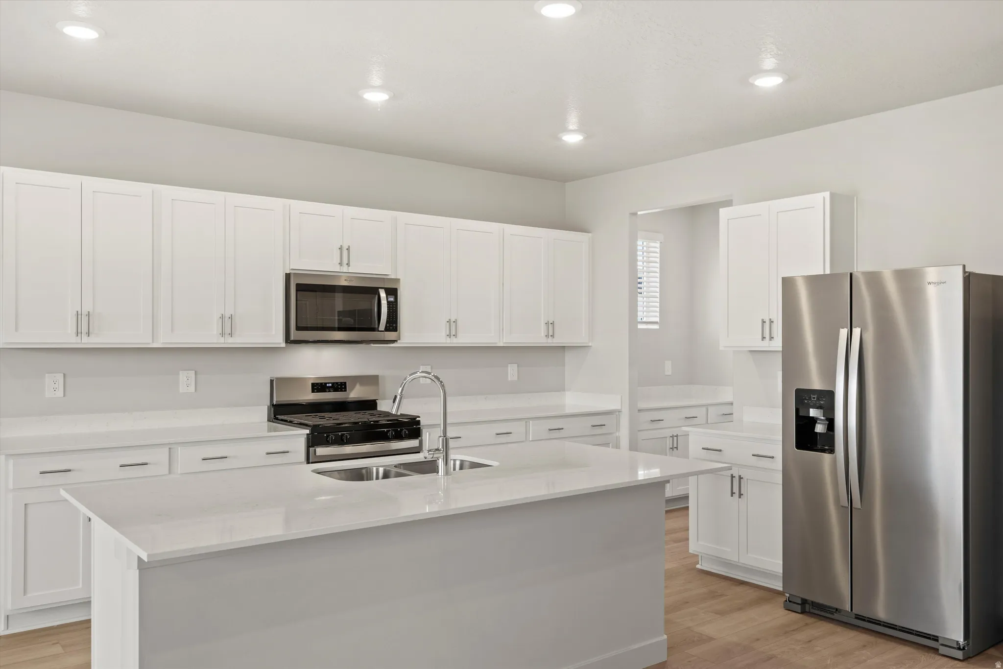 Modern kitchen featuring an island with an integrated sink, white cabinetry, stainless steel appliances, and recessed lighting