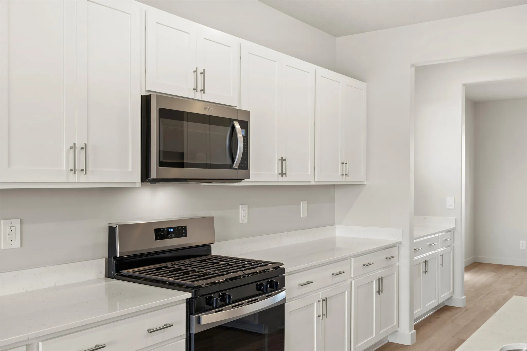 Kitchen featuring white shaker-style cabinetry, stainless steel range and microwave, light-toned countertops, and wood-finish flooring