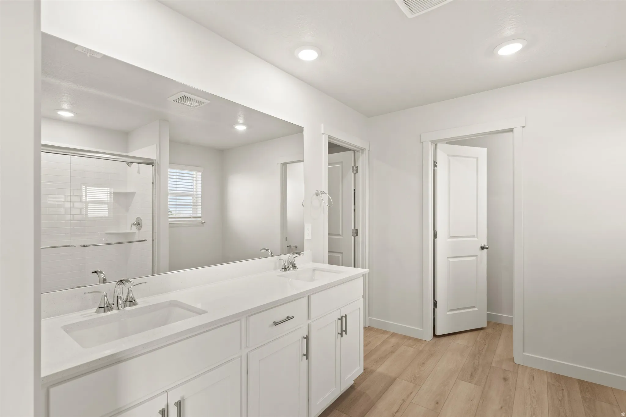 Bathroom featuring a double vanity with white cabinetry and integrated sinks, a large wall-mounted mirror, and wood-finish flooring