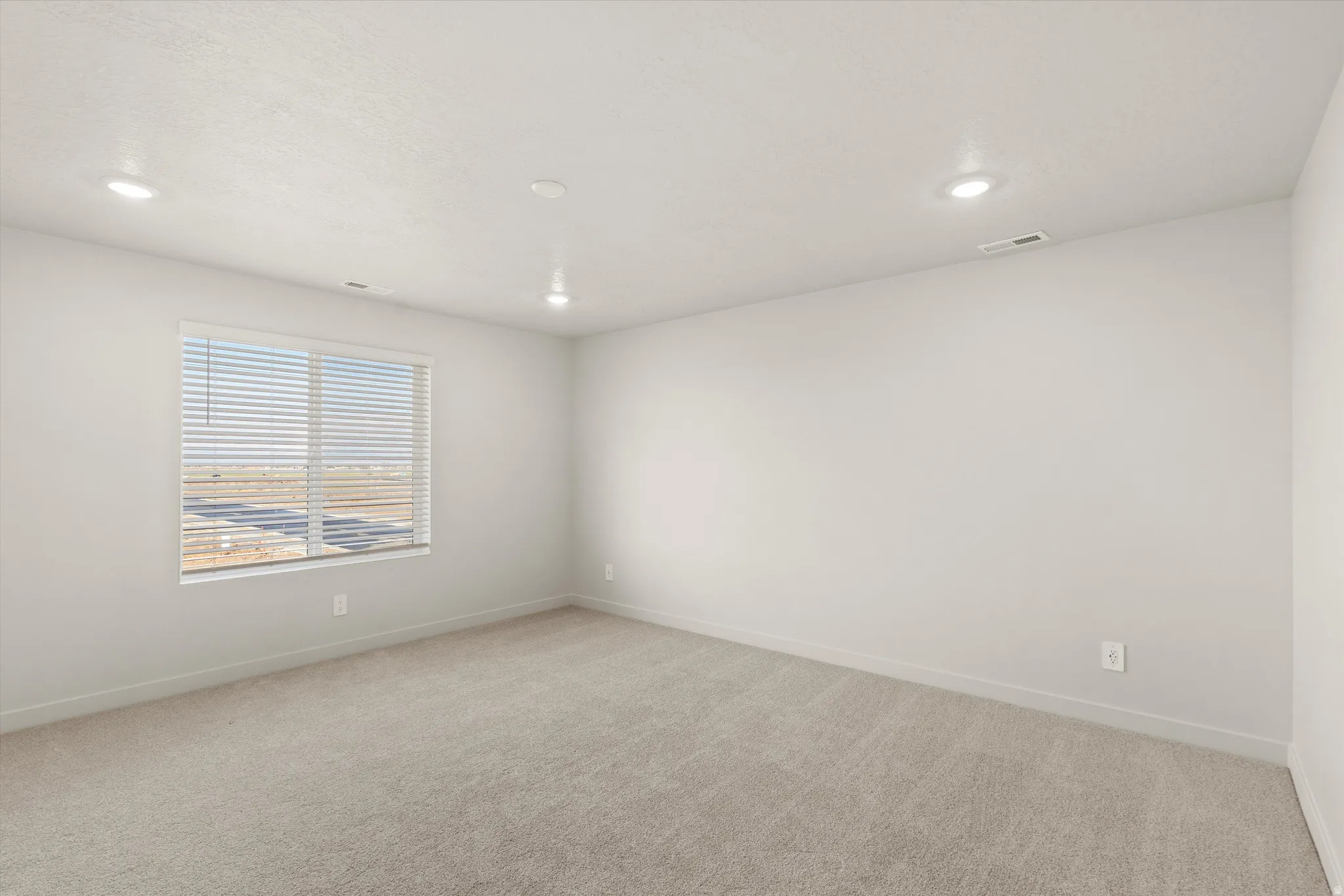Carpeted interior space featuring a large window with blinds, recessed ceiling lighting, light-toned walls, and white trim