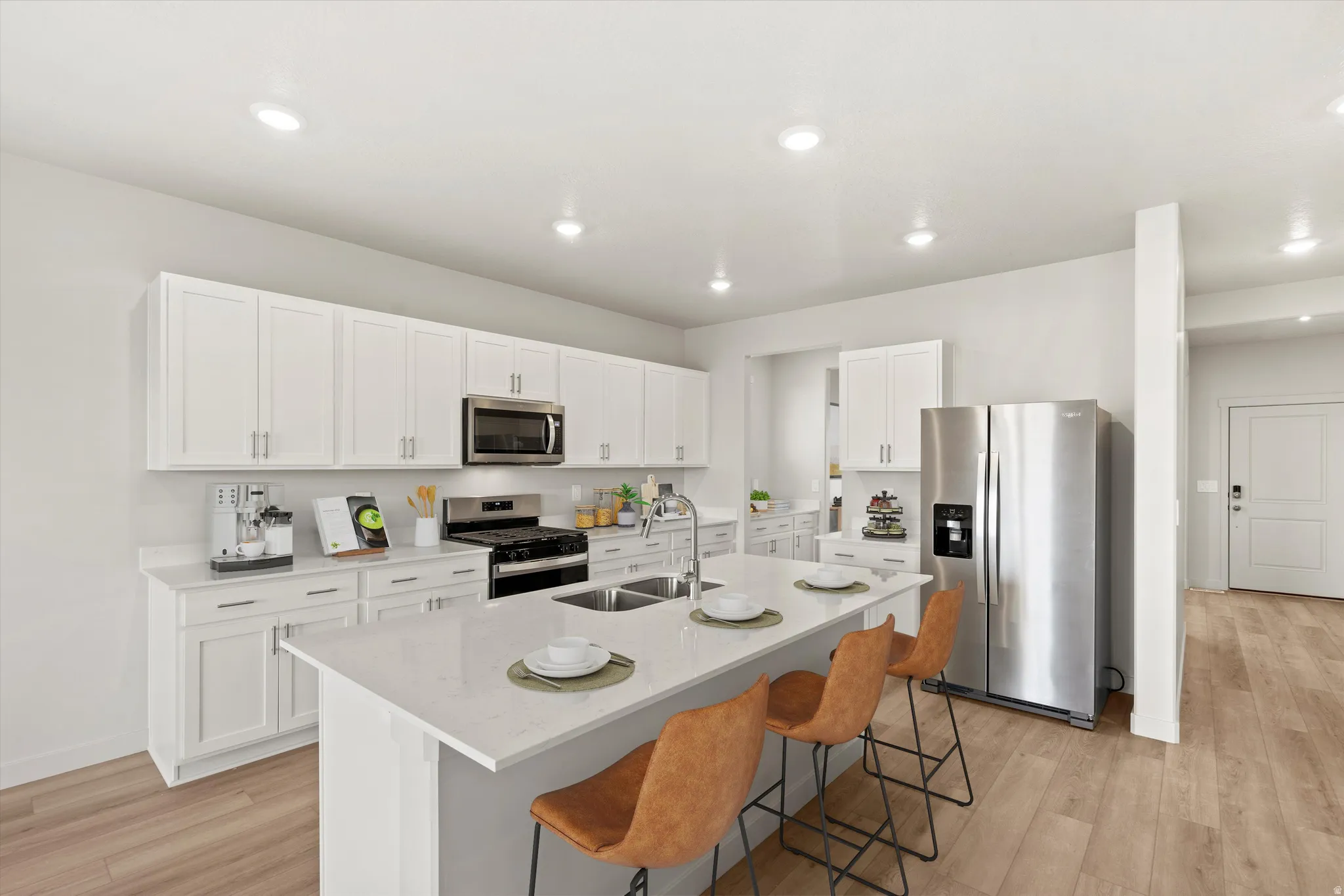 Modern kitchen featuring white shaker cabinetry, stainless steel appliances, a center island with sink, quartz countertops, and wood-finish flooring