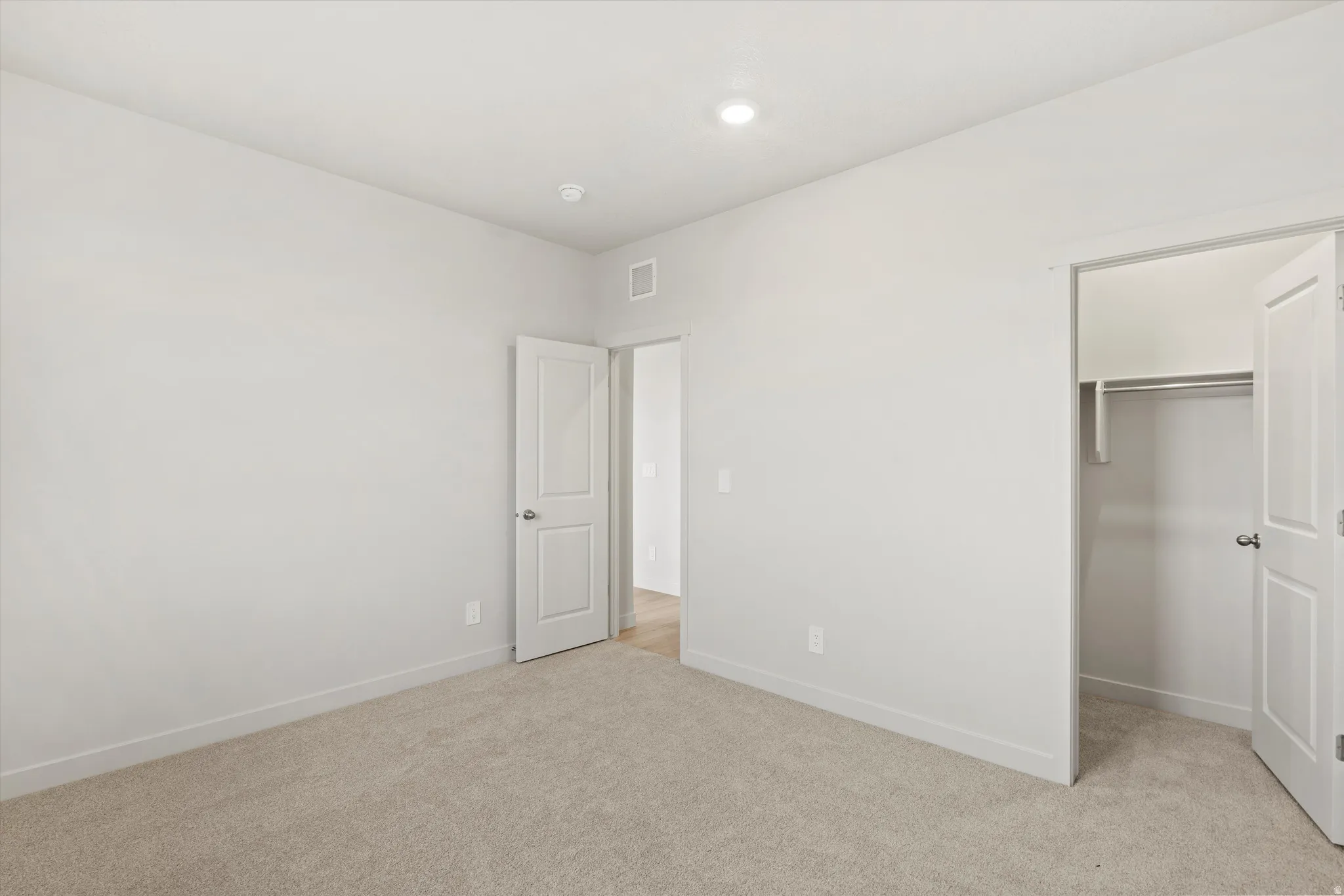 Neutral-toned carpeting paired with white walls, a built-in closet with a hanging rod and shelf, and modern white interior doors