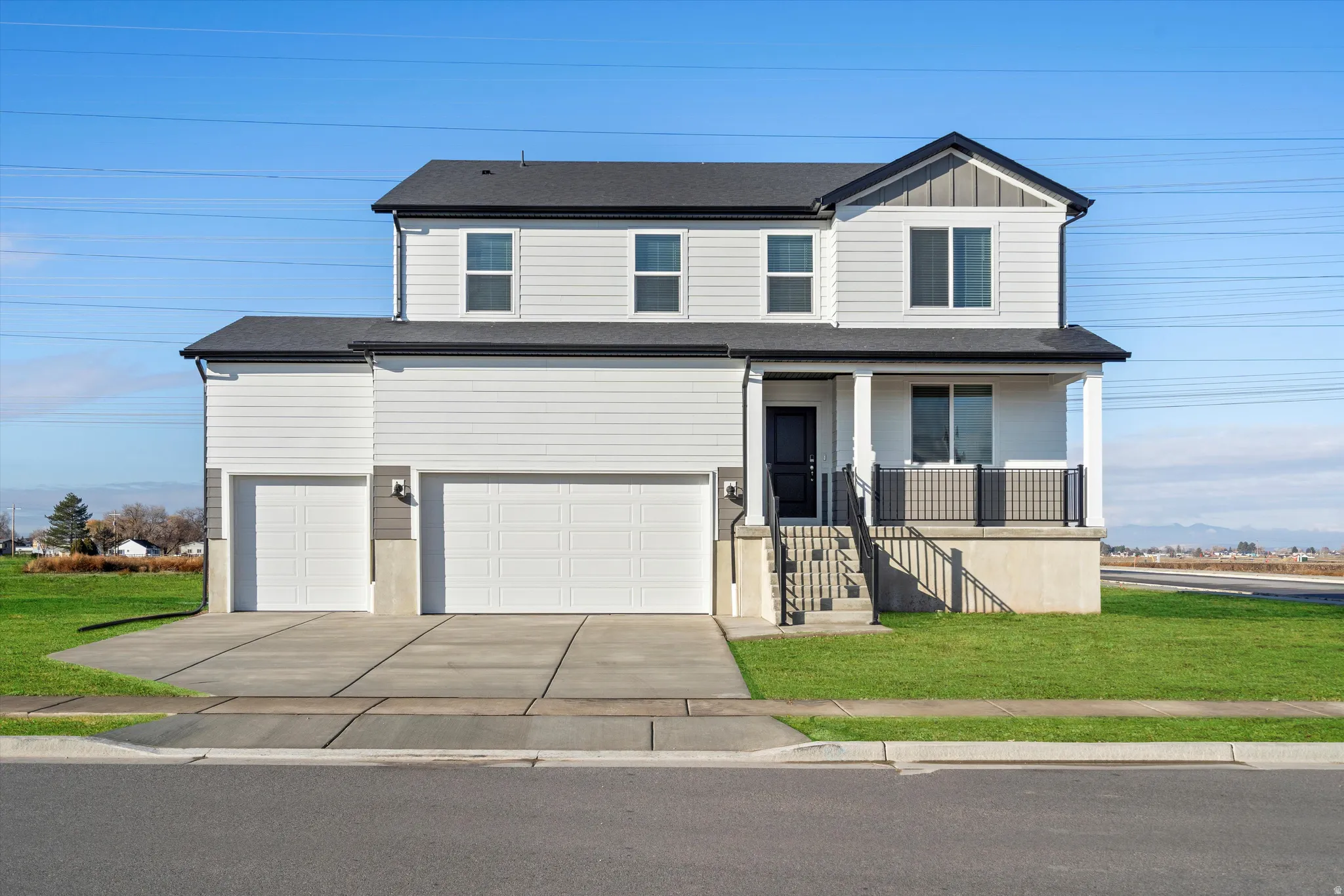 Two-story residence featuring a covered front porch with black railings, a black front door, and a two-car garage with white doors