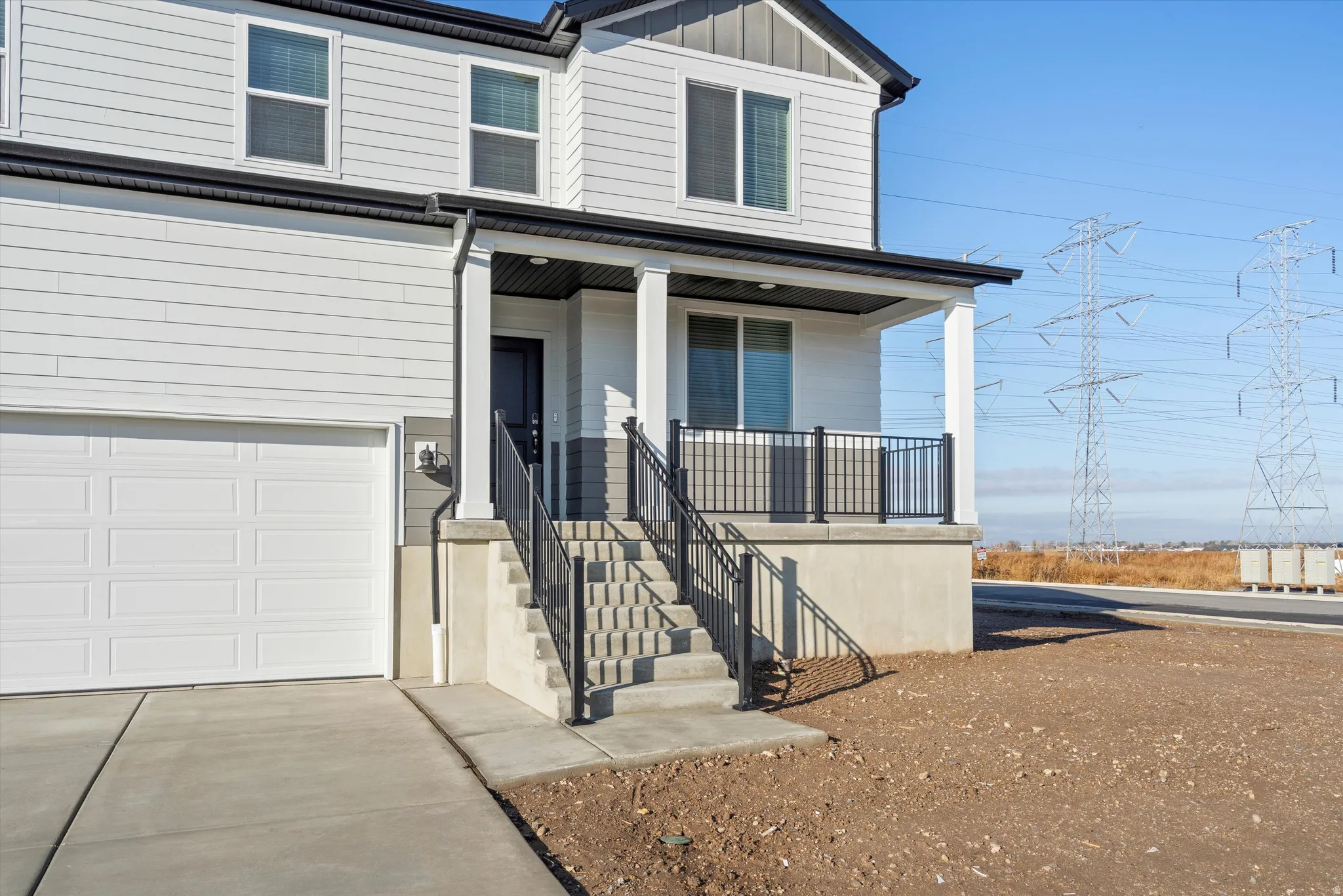 Two-story siding exterior featuring a covered porch with white columns, concrete steps, and dark metal railings