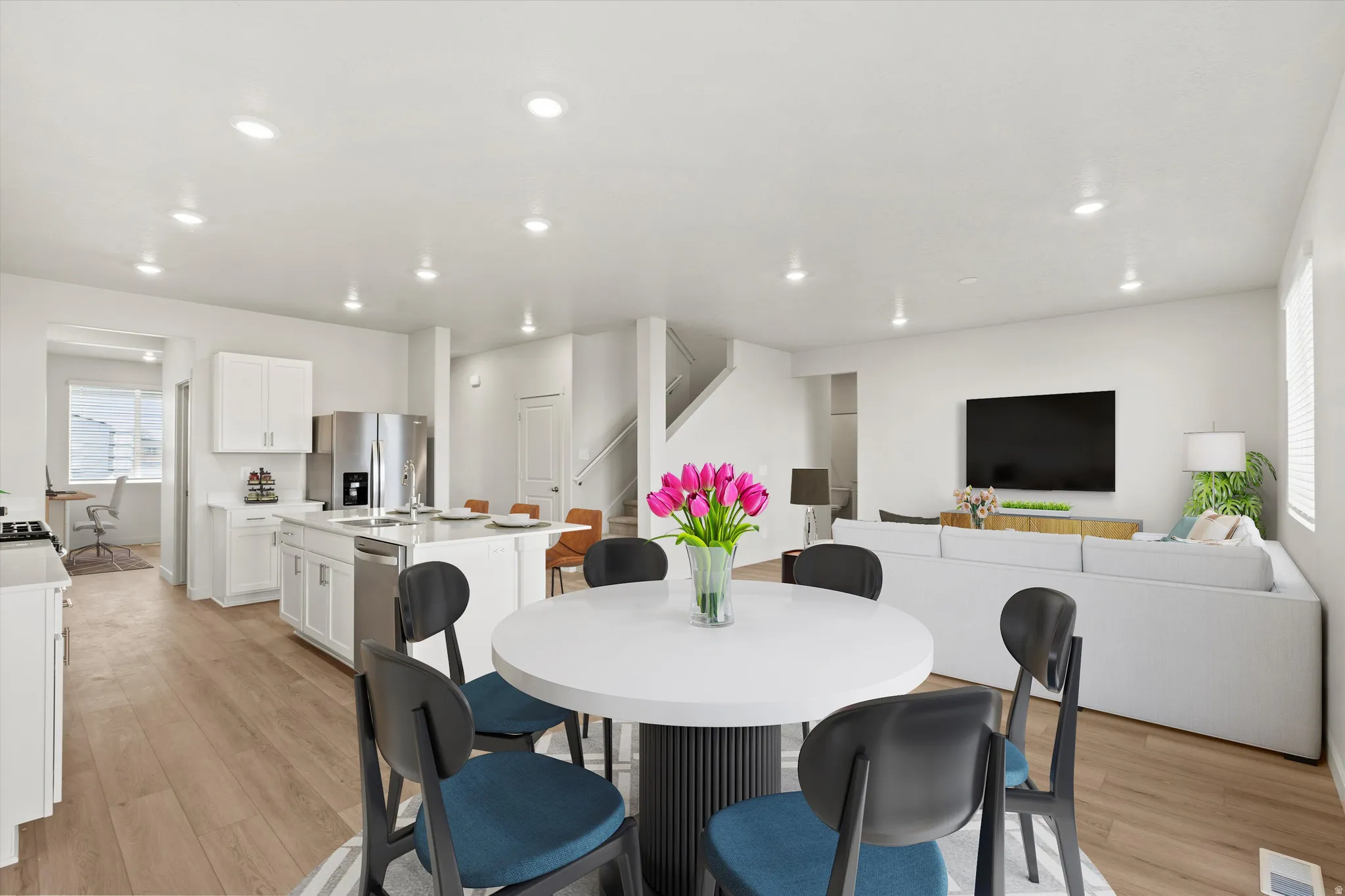 Open-concept living area featuring wood-finish flooring, recessed lighting, and a white kitchen with stainless steel appliances