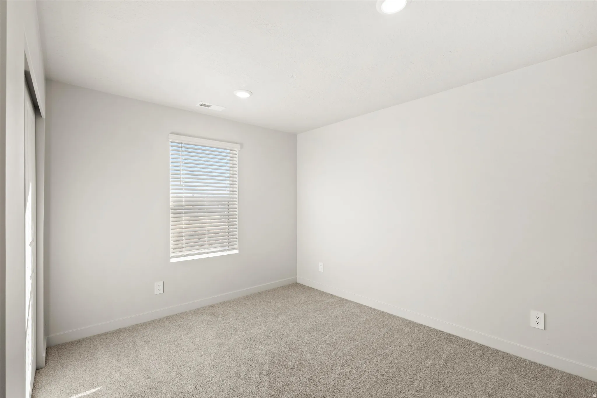 Neutral tone wall finishes, recessed ceiling lighting, light-toned carpet flooring, a window with horizontal blinds, and a sliding glass door