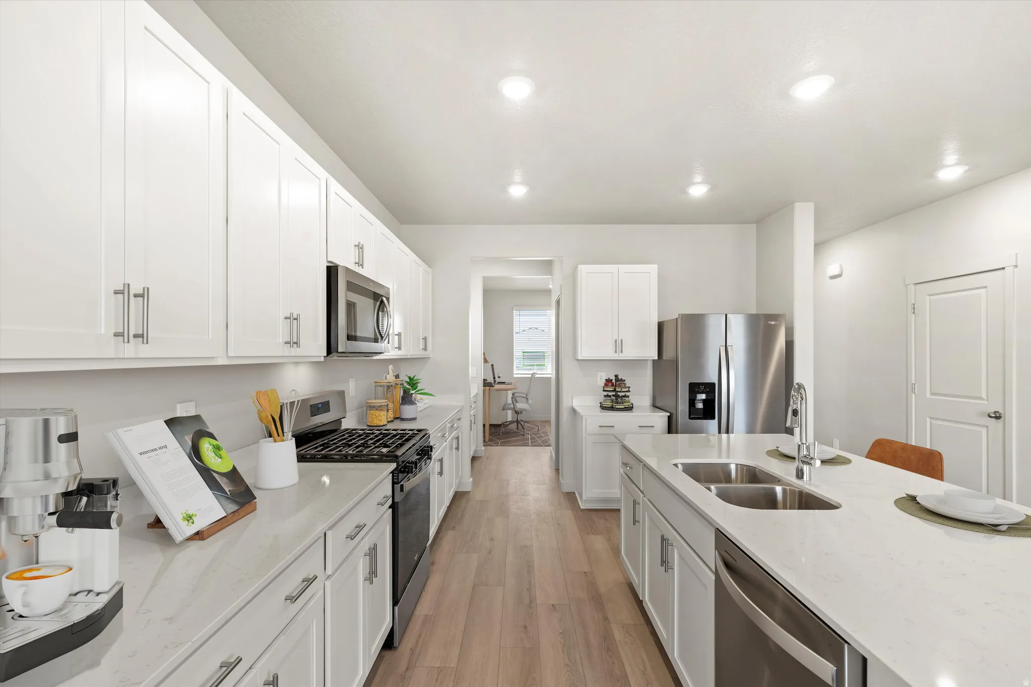 Modern kitchen with extensive white cabinetry, light countertops, wood-finish flooring, stainless steel appliances, and a central island with a double basin sink