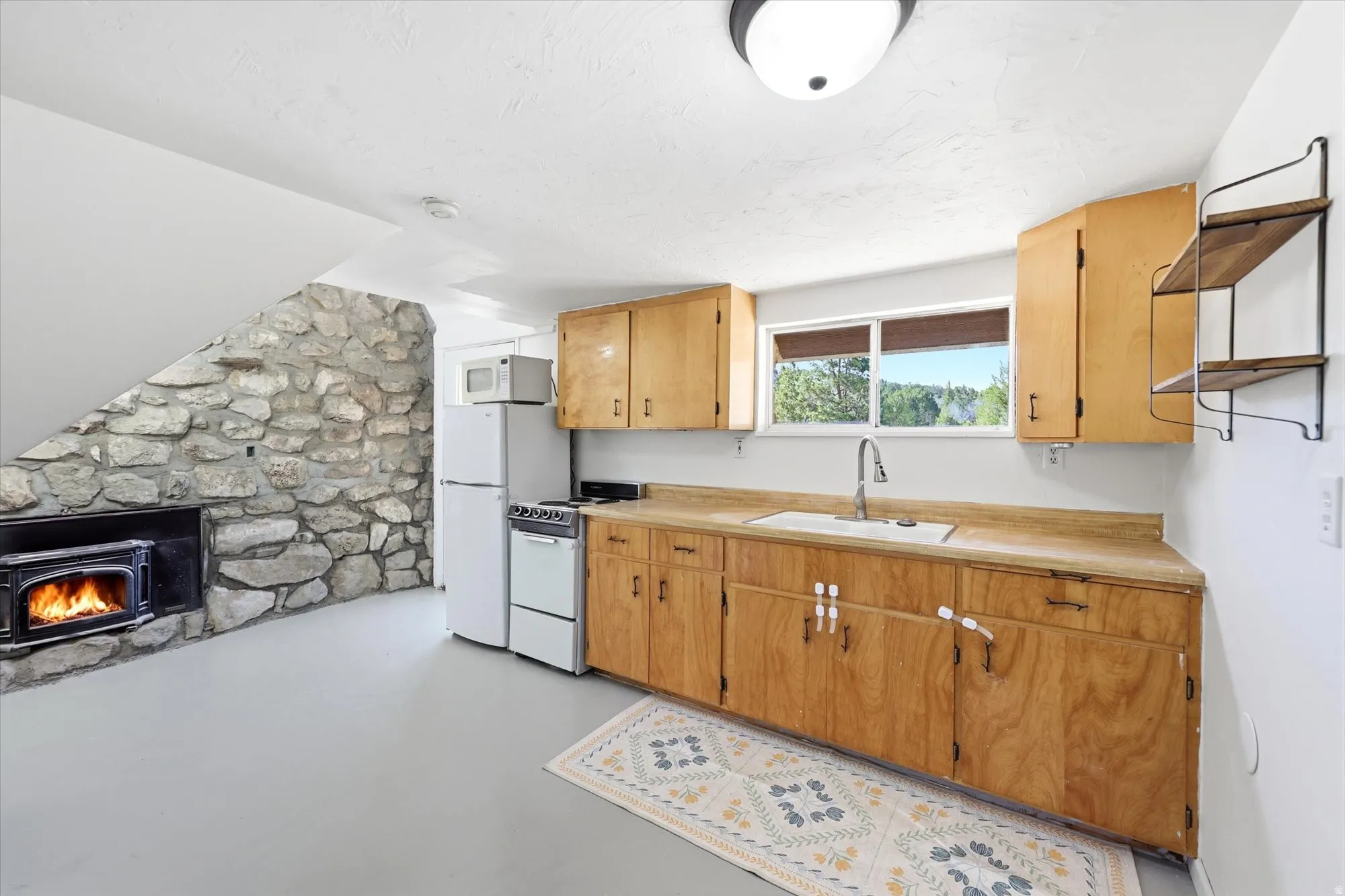Kitchen featuring light countertops, concrete floors, white appliances, and a lit fireplace