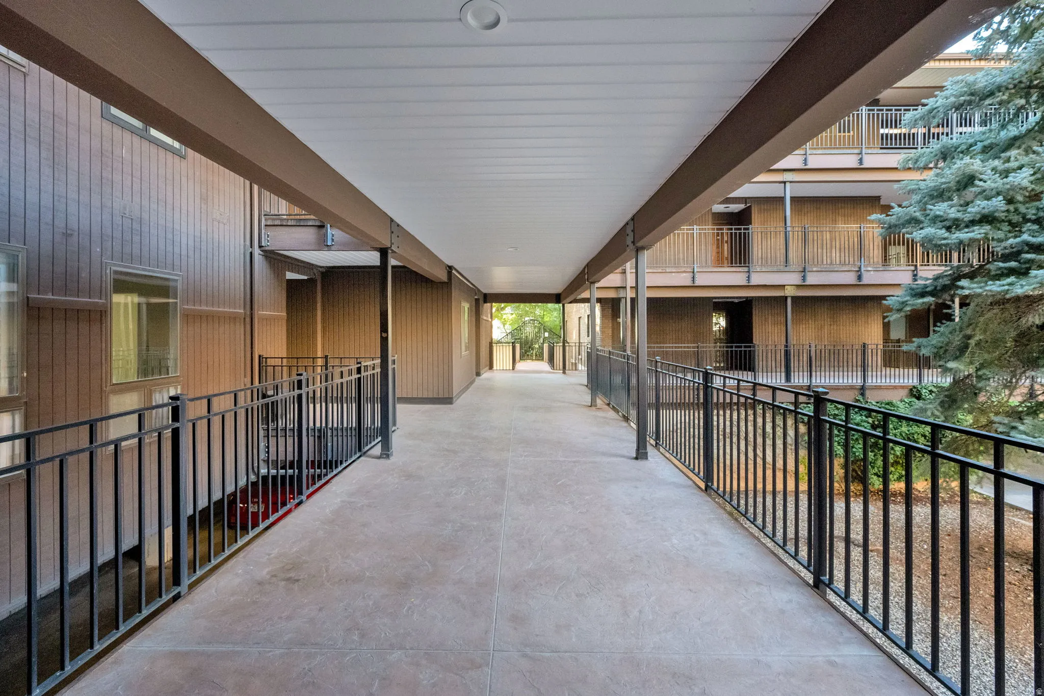 Covered exterior walkway featuring a concrete surface and black metal railings