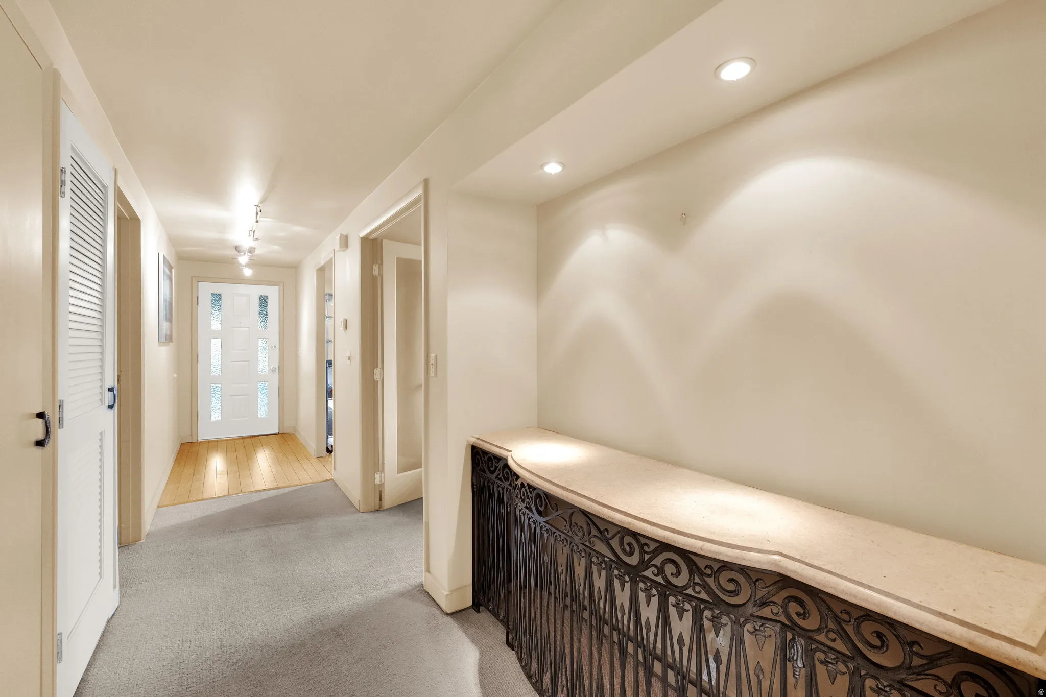Foyer featuring a decorative wrought iron console with a light-colored countertop, recessed lighting, track lighting, a white paneled entry door with frosted glass inserts, and a combination of carpet and wood-finish flooring