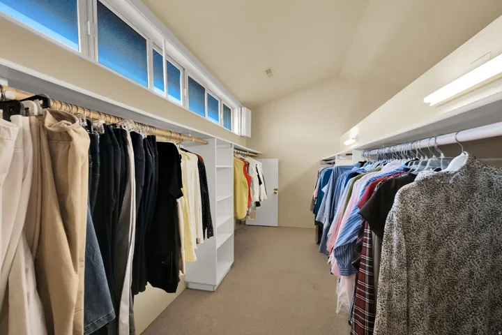 Spacious walk-in closet featuring extensive built-in shelving, multiple clothing rods, and high transom windows