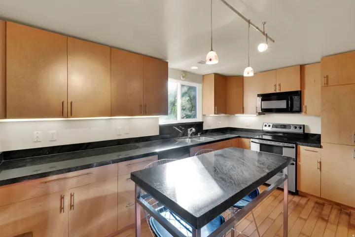 Modern kitchen featuring extensive wood cabinetry, dark stone countertops, and wood-finish flooring