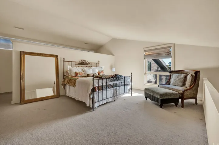 Spacious carpeted room featuring vaulted ceilings, a window with exterior architectural elements visible, and a half-wall partition