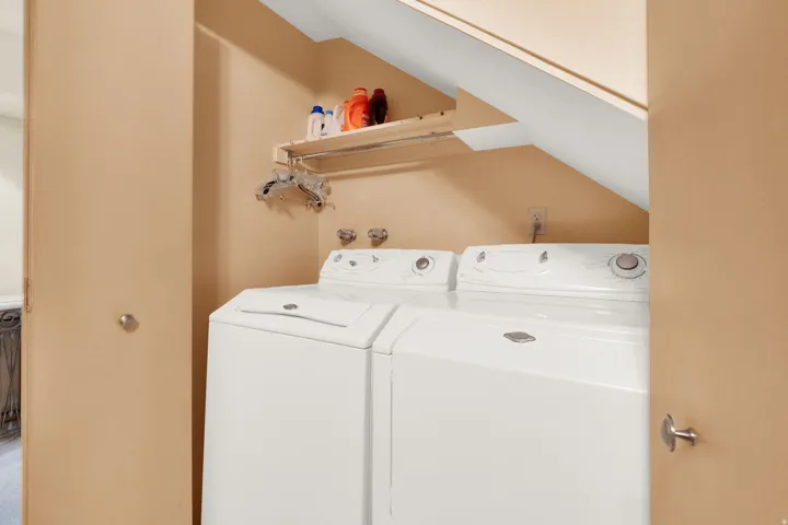 Dedicated laundry area featuring a white washing machine and dryer, a wall-mounted storage shelf, and a built-in hanging rod