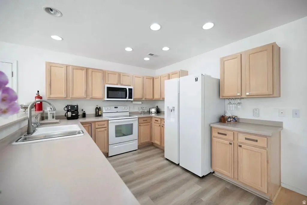 Kitchen featuring light wood cabinetry, white appliances, recessed lighting, wood-finish flooring, and a stainless steel sink with a high-arc faucet