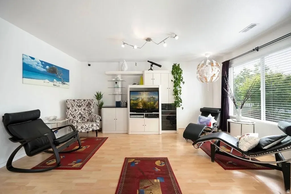 Bright living area featuring wood-finish flooring, white walls, and a large window with horizontal blinds