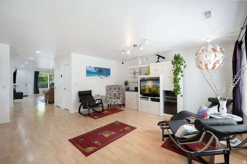 Spacious living area featuring light wood-finish flooring, recessed lighting, white walls, and a built-in media console with display shelving