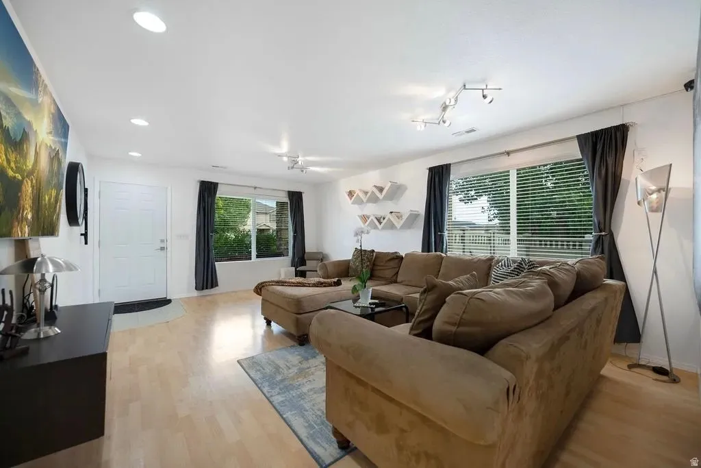 Open-concept living area featuring light wood-finish flooring, recessed lighting, and large windows with blinds