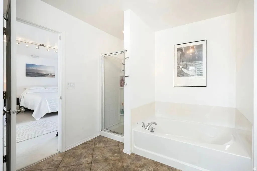 Bathroom featuring a built-in tub, a glass-enclosed shower, and neutral tile flooring