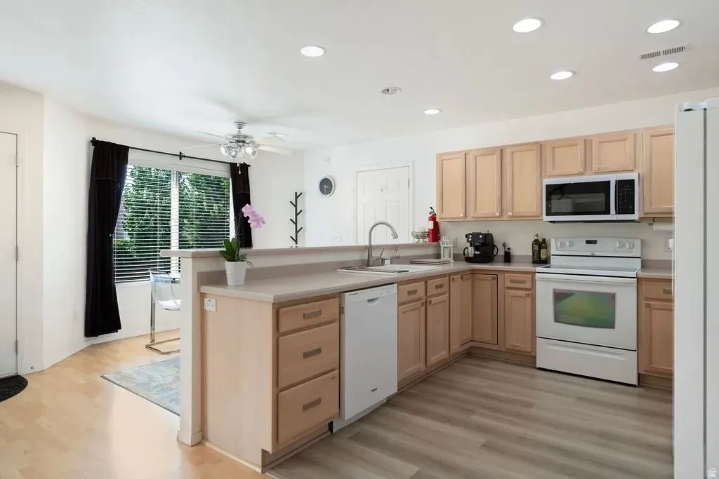 Kitchen featuring wood-finish flooring, light wood cabinetry, white appliances, and recessed lighting