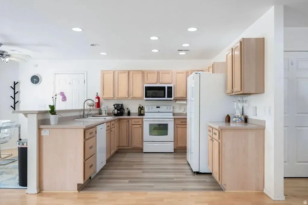 Kitchen featuring wood-finish cabinetry, light-toned countertops, white appliances, recessed lighting, and wood-finish flooring