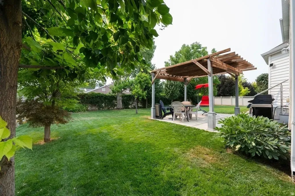 Expansive backyard with a manicured lawn, featuring a concrete patio, a wooden pergola, and mature trees