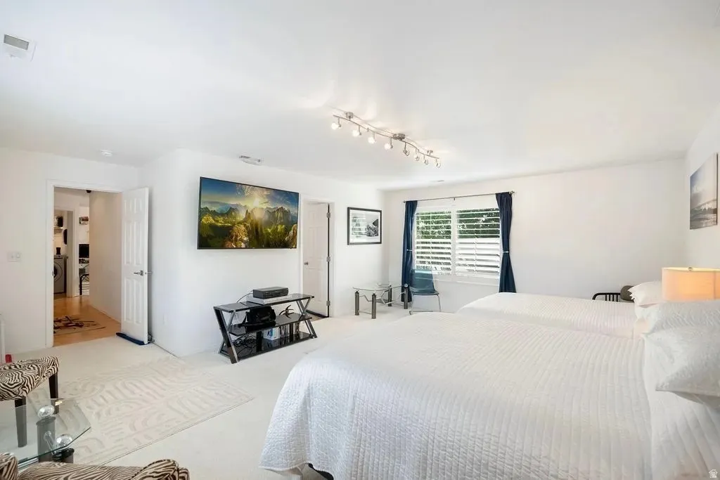 White-painted room featuring light-colored carpet, a window with white louvered shutters, and a wall-mounted television