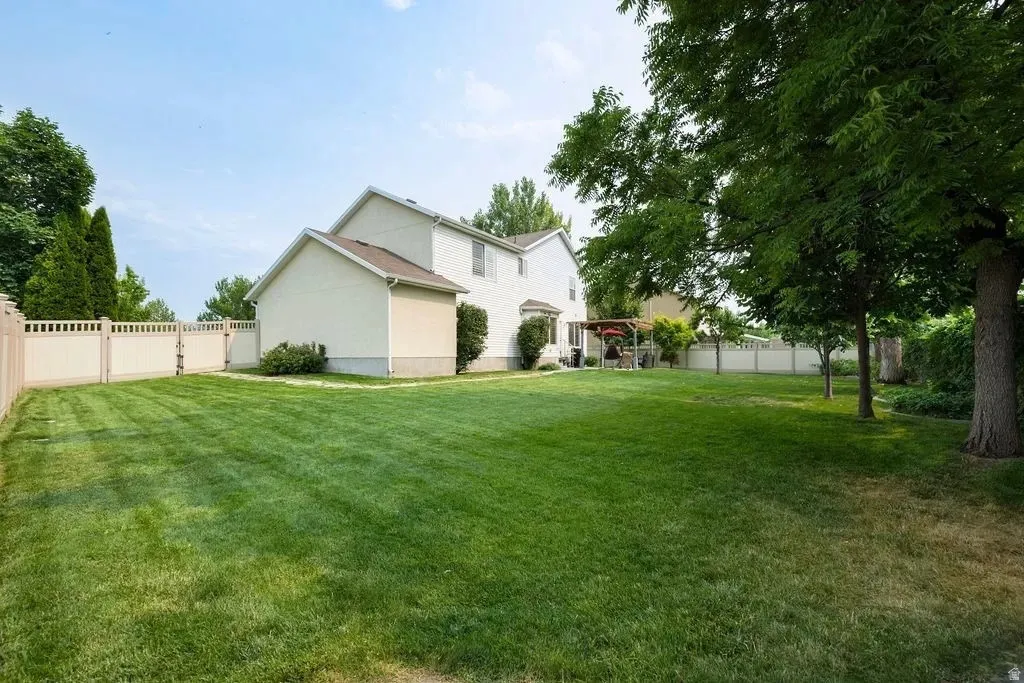 Expansive backyard featuring a lush lawn, established trees, perimeter fencing, and a covered patio area