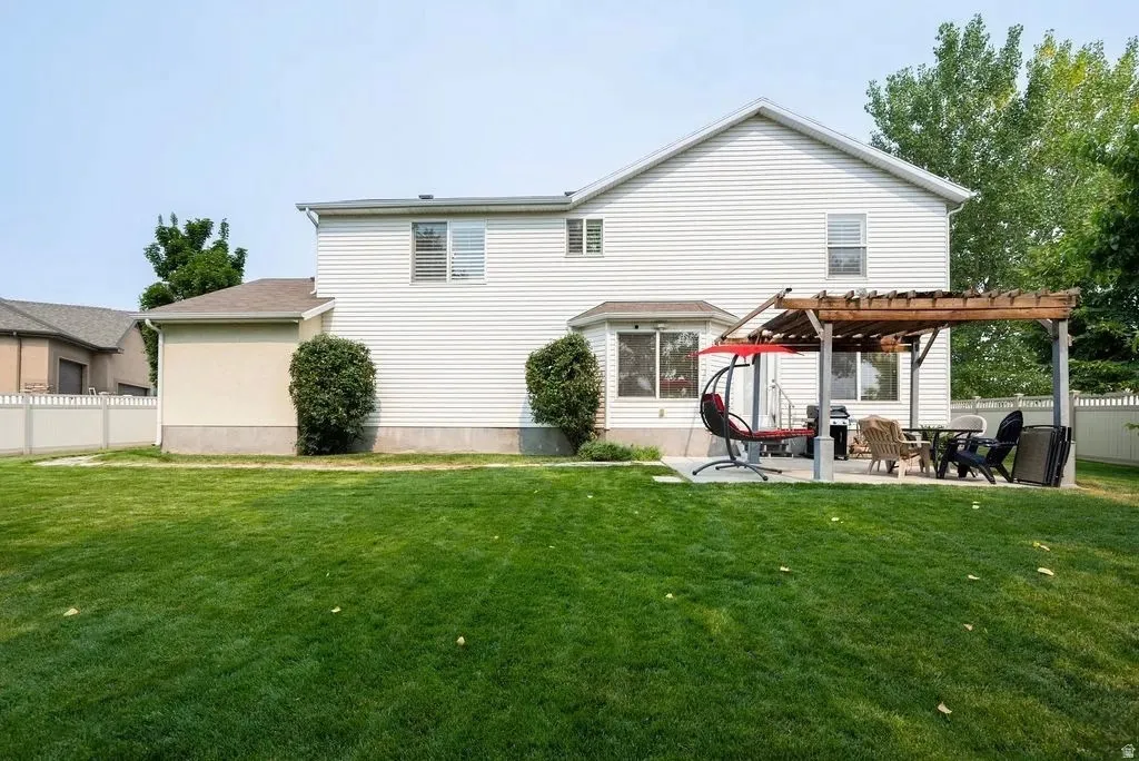 Expansive backyard featuring a large green lawn, a concrete patio, and a wooden pergola structure