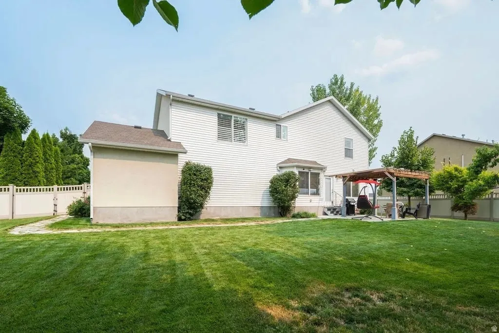 Expansive lawn featuring a concrete patio with a wood pergola, bay window, and a privacy fence