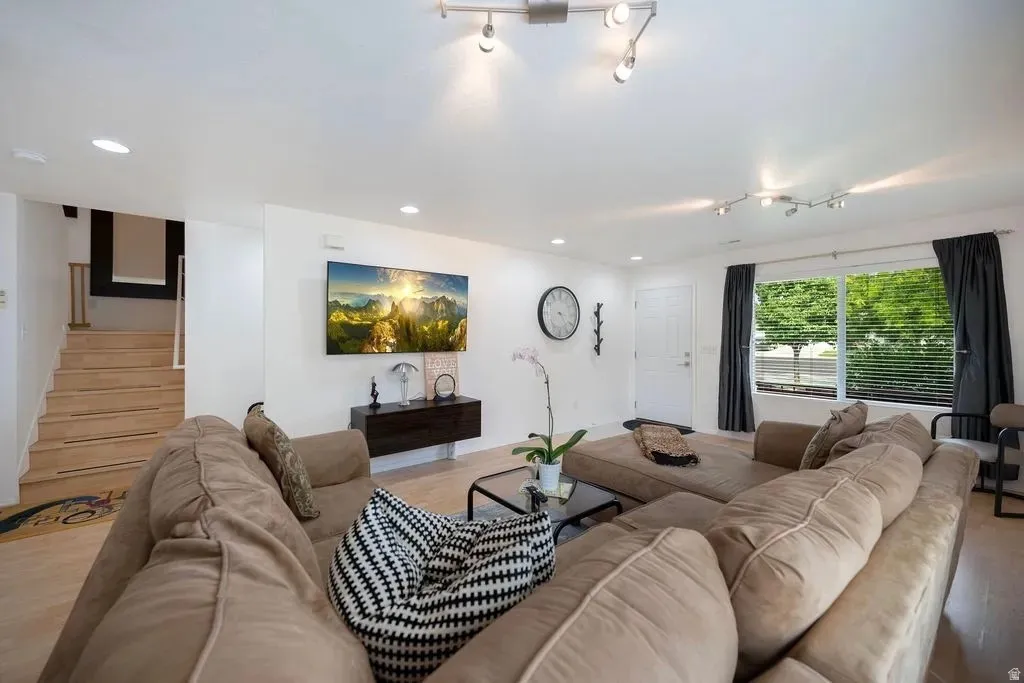 Living area featuring light wood-finish flooring, white walls, and a large window with blinds
