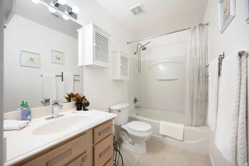 Bathroom featuring a wood-finish vanity with an integrated sink and chrome faucet, a white acrylic tub and shower combination, a white toilet, and tile flooring